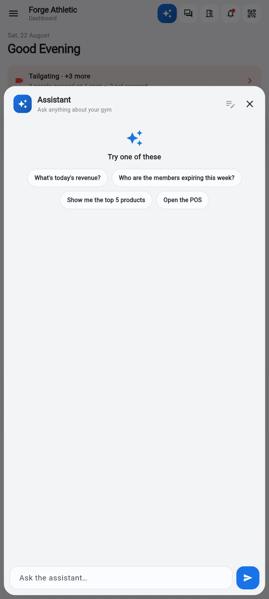 The Assistant sheet open over the dashboard: header 'Assistant — Ask anything about your gym', a sparkle icon above 'Try one of these', and the suggestion chips What's today's revenue?, Who are the members expiring this week?, Show me the top 5 products and Open the POS, with the 'Ask the assistant…' field at the bottom